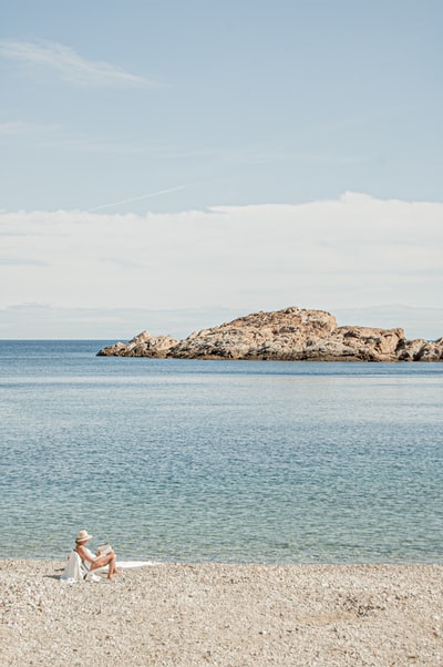 White shirt woman sitting on a rock near the waters during the day
